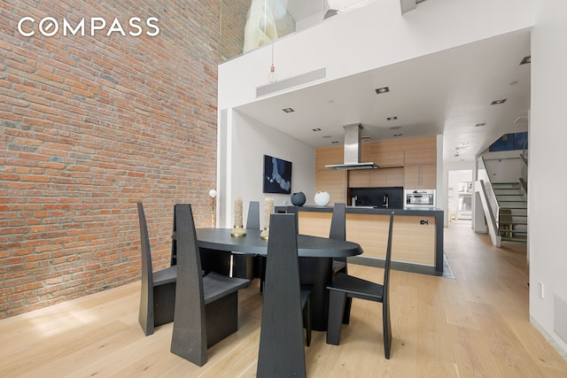 dining area featuring brick wall, a towering ceiling, and light hardwood / wood-style floors