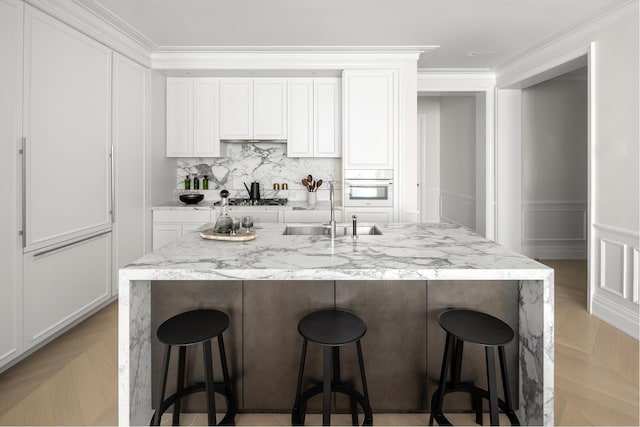 kitchen with a breakfast bar area, oven, white cabinetry, and sink