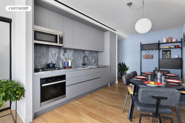 kitchen featuring light hardwood / wood-style floors, gray cabinets, stainless steel appliances, and tasteful backsplash