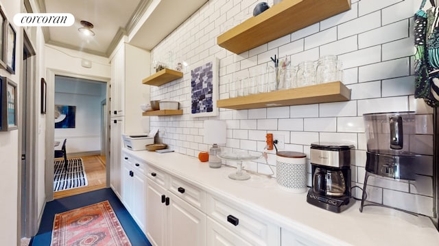 kitchen with backsplash, dark hardwood / wood-style floors, white cabinetry, and crown molding