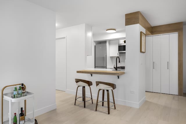 kitchen featuring light hardwood / wood-style floors, white cabinets, a breakfast bar, kitchen peninsula, and stainless steel appliances