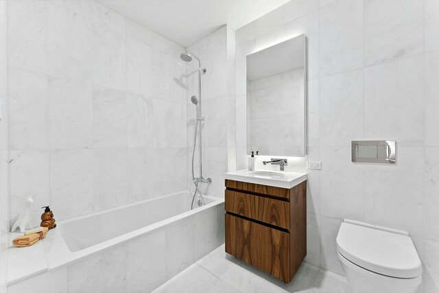 full bathroom with tile walls, tiled shower / bath combo, vanity, and toilet