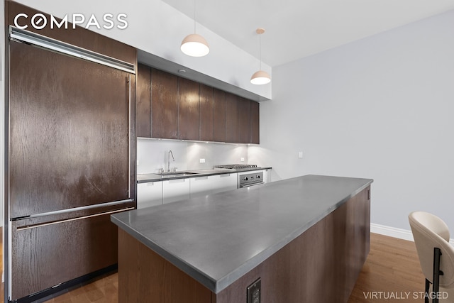 kitchen with decorative light fixtures, dark wood-type flooring, a center island, sink, and dark brown cabinetry