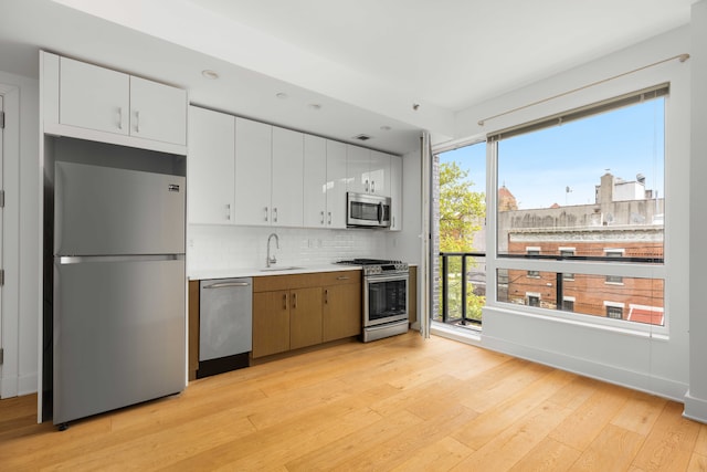 kitchen featuring light wood-type flooring, tasteful backsplash, sink, white cabinets, and stainless steel appliances