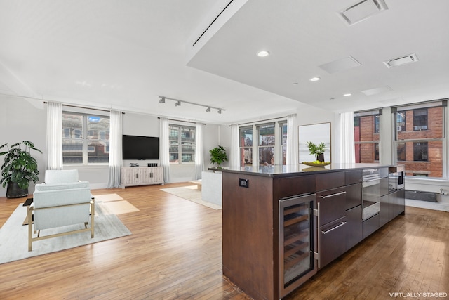 kitchen featuring a center island, track lighting, wine cooler, light wood-type flooring, and dark brown cabinetry