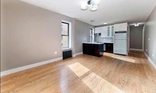 kitchen featuring white cabinets, white refrigerator, radiator, a center island, and light wood-type flooring