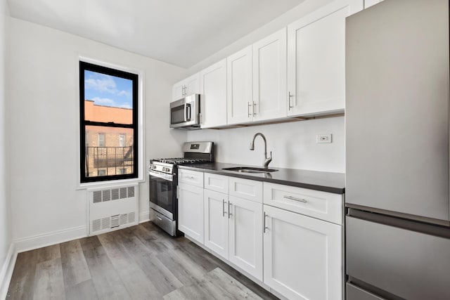 kitchen with radiator heating unit, sink, white cabinetry, and stainless steel appliances