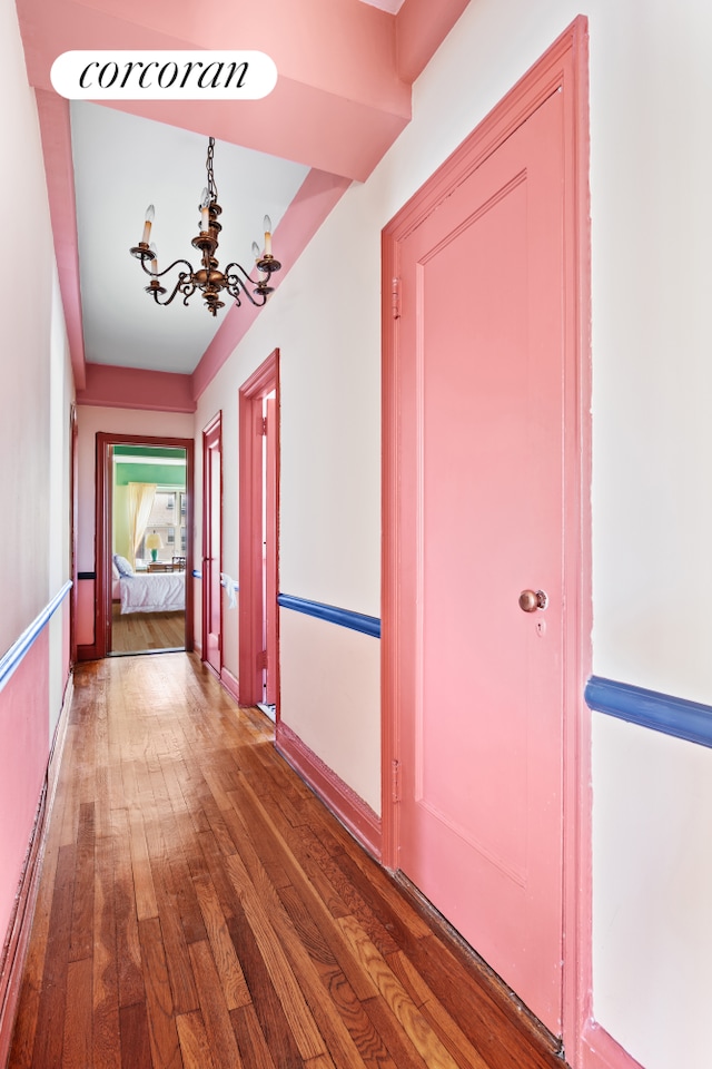 corridor with wood-type flooring and a chandelier