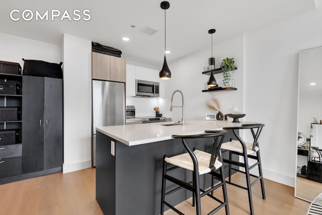 kitchen featuring hanging light fixtures, sink, light hardwood / wood-style flooring, stainless steel appliances, and a breakfast bar