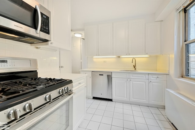 kitchen with sink, white cabinets, decorative backsplash, appliances with stainless steel finishes, and light tile patterned floors