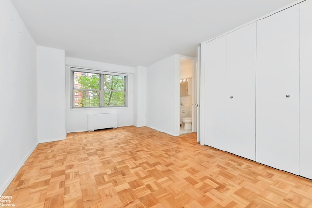 unfurnished bedroom featuring radiator heating unit, ensuite bathroom, and light parquet flooring