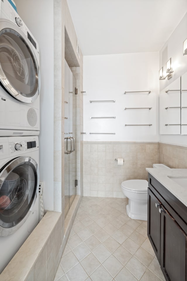 bathroom featuring tile patterned floors, stacked washer / drying machine, toilet, vanity, and an enclosed shower