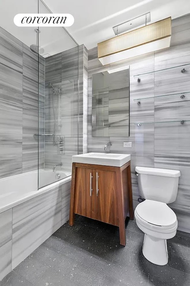 full bathroom with vanity, tile walls, toilet, and combined bath / shower with glass door