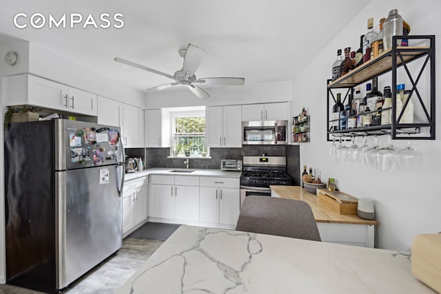 kitchen with white cabinetry, stainless steel appliances, backsplash, light stone countertops, and ceiling fan