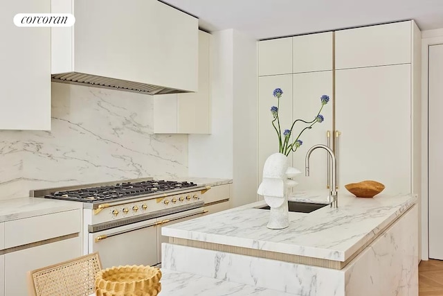 kitchen featuring stainless steel range, a center island with sink, backsplash, and white cabinetry