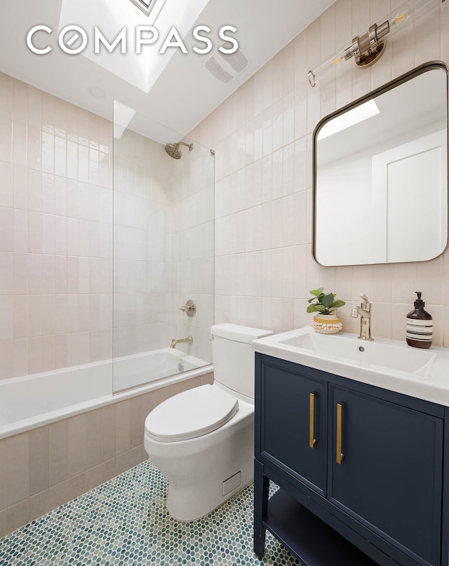 full bathroom with tile patterned flooring, tiled shower / bath combo, toilet, and tile walls