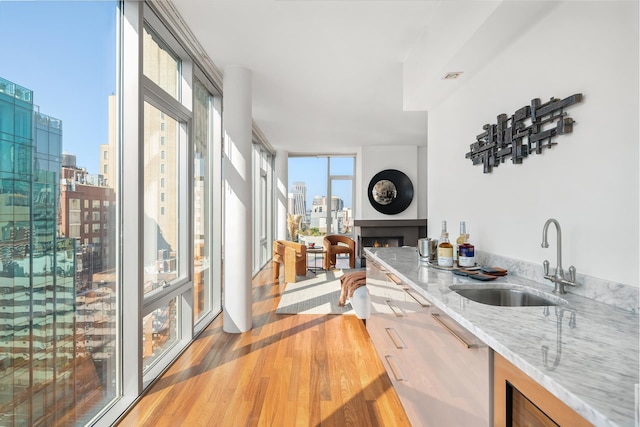 kitchen with light stone counters, a wall of windows, hardwood / wood-style floors, and sink