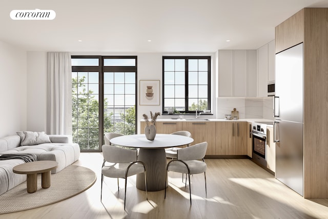 kitchen featuring sink, backsplash, stainless steel appliances, light brown cabinetry, and light hardwood / wood-style floors