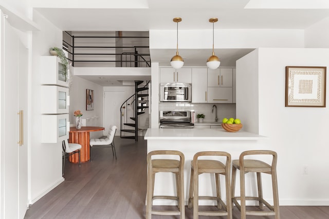 kitchen with stainless steel appliances, kitchen peninsula, decorative light fixtures, and dark hardwood / wood-style flooring