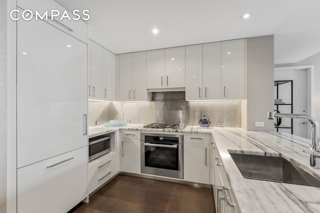 kitchen with sink, dark wood-type flooring, white cabinetry, appliances with stainless steel finishes, and light stone countertops