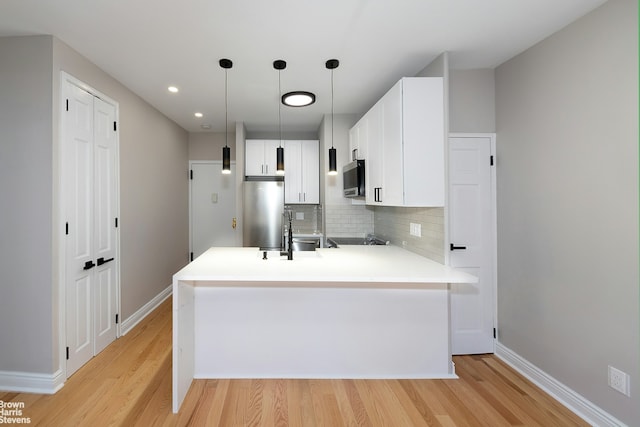 kitchen with backsplash, stainless steel appliances, decorative light fixtures, light hardwood / wood-style flooring, and white cabinetry