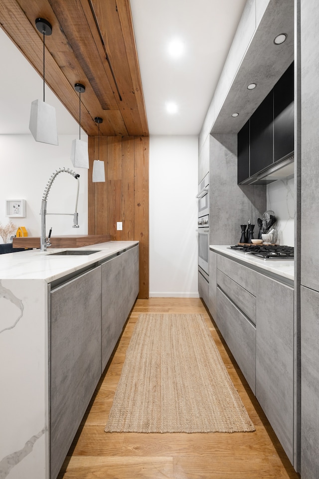 kitchen with sink, decorative light fixtures, stainless steel appliances, light wood-type flooring, and a kitchen bar