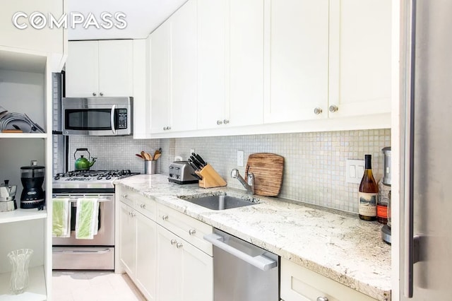 kitchen featuring stainless steel appliances, white cabinetry, light stone counters, and sink