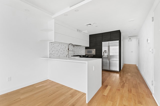 kitchen featuring light wood-type flooring, backsplash, kitchen peninsula, and built in appliances