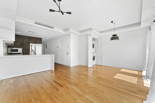 unfurnished living room with a tray ceiling, light hardwood / wood-style floors, and stacked washing maching and dryer