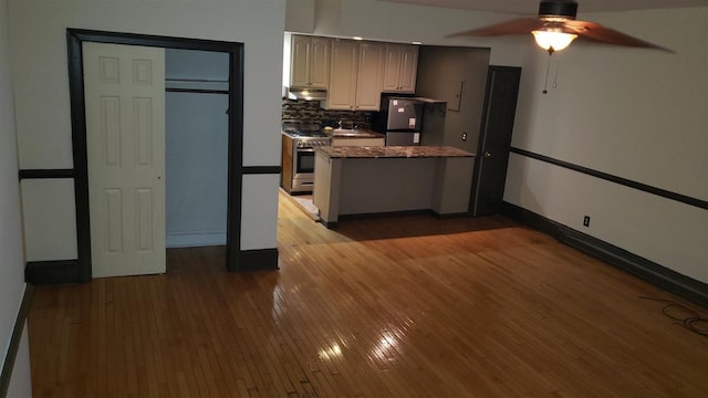 kitchen with stainless steel range, black fridge, hardwood / wood-style floors, and tasteful backsplash