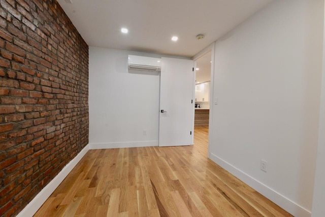 empty room with an AC wall unit, brick wall, and light hardwood / wood-style floors