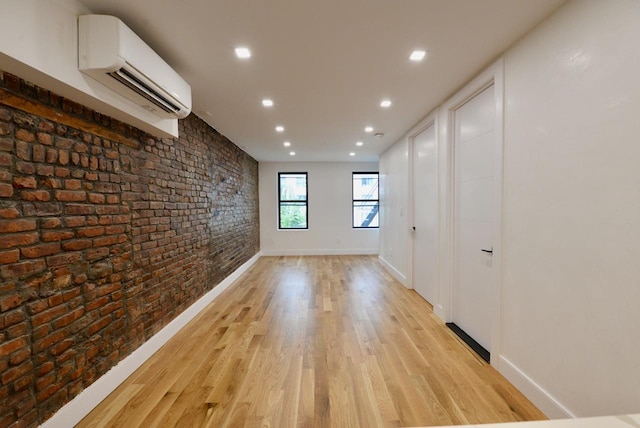 spare room with an AC wall unit, brick wall, and light hardwood / wood-style floors