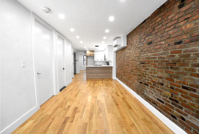 hall with a wall unit AC, brick wall, and light wood-type flooring