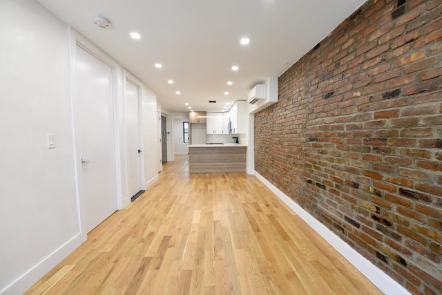 corridor featuring an AC wall unit, brick wall, and light hardwood / wood-style flooring