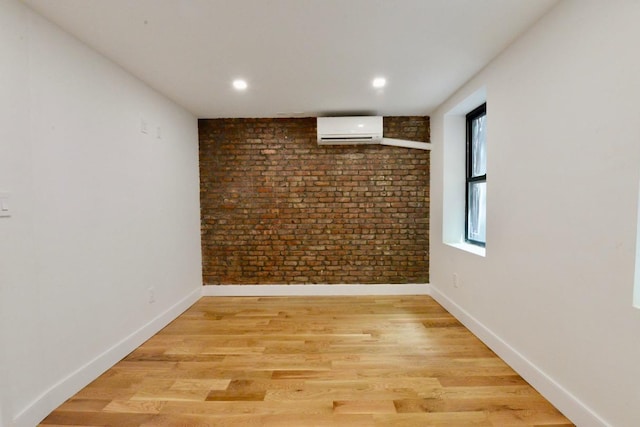 empty room featuring a wall mounted air conditioner, light hardwood / wood-style flooring, and brick wall