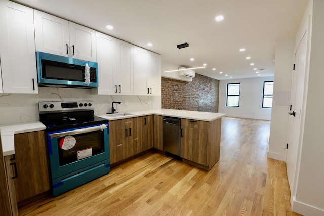 kitchen with tasteful backsplash, appliances with stainless steel finishes, white cabinetry, light hardwood / wood-style flooring, and decorative light fixtures