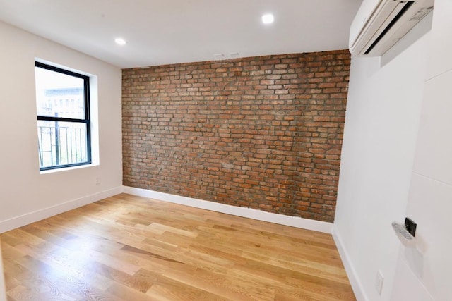 unfurnished room featuring a wall mounted AC, wood-type flooring, and brick wall