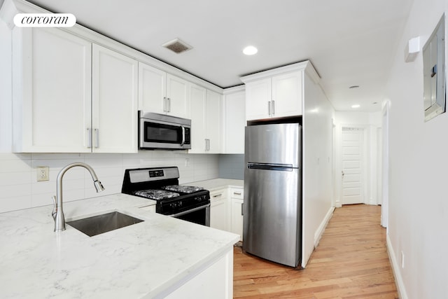 kitchen featuring light stone counters, sink, white cabinetry, appliances with stainless steel finishes, and light wood-type flooring