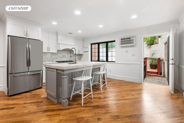 kitchen with stainless steel fridge, a kitchen island with sink, white cabinetry, a kitchen breakfast bar, and dark hardwood / wood-style flooring