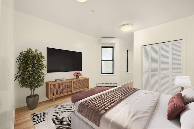 bedroom featuring a closet, a wall mounted AC, radiator heating unit, and light wood-type flooring