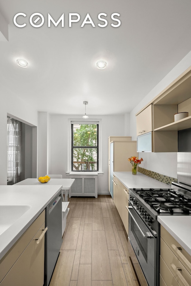 kitchen with stainless steel appliances, cream cabinets, radiator heating unit, light hardwood / wood-style floors, and hanging light fixtures