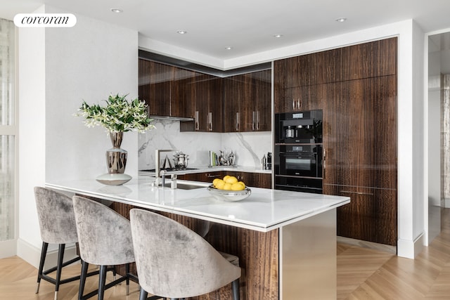 kitchen featuring decorative backsplash, kitchen peninsula, a breakfast bar area, and light parquet floors