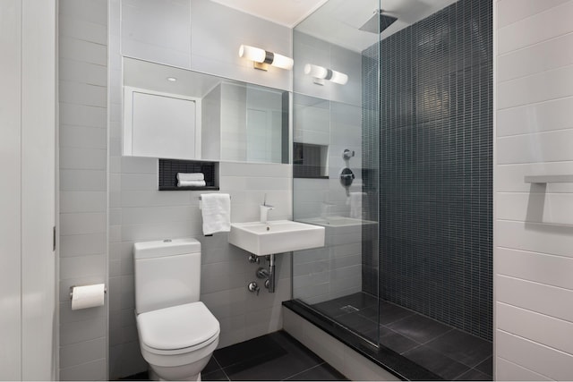 bathroom with toilet, sink, a tile shower, and tile walls