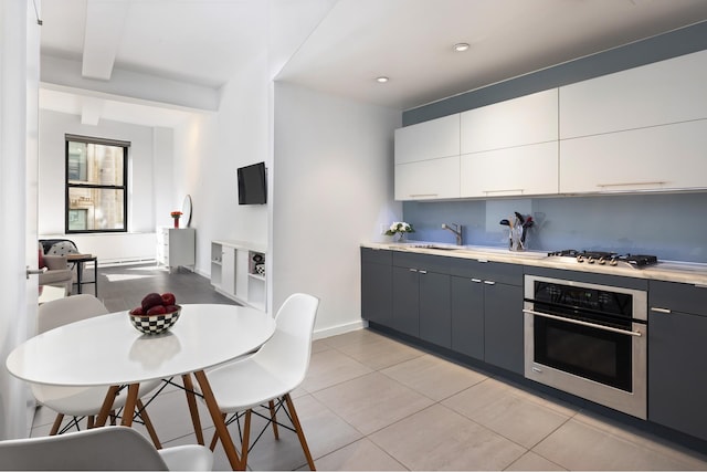 kitchen with beam ceiling, light tile patterned floors, white cabinetry, sink, and stainless steel appliances