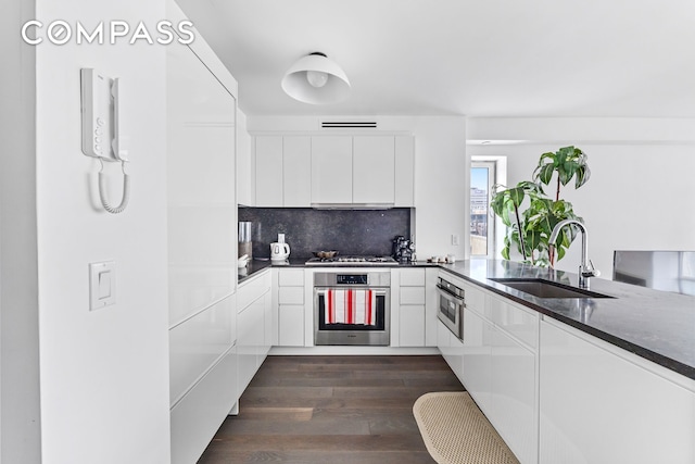 kitchen with appliances with stainless steel finishes, dark stone counters, dark wood-type flooring, sink, and white cabinets