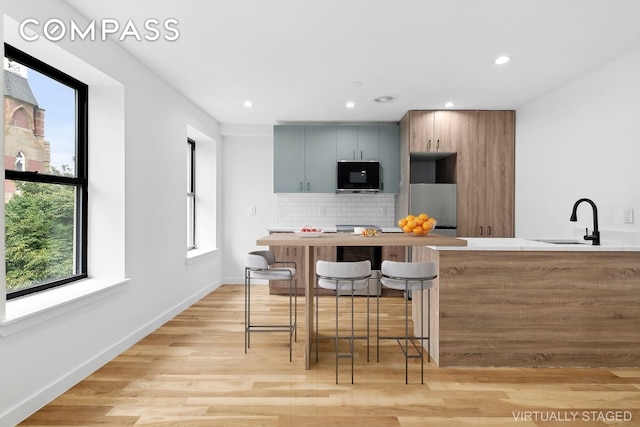 kitchen featuring sink, gray cabinetry, a kitchen bar, stainless steel appliances, and light hardwood / wood-style floors