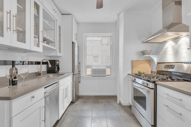 kitchen with wall chimney range hood, stainless steel appliances, sink, light tile patterned flooring, and white cabinets