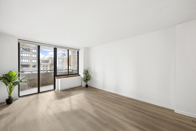 empty room with hardwood / wood-style floors, a wall of windows, and radiator