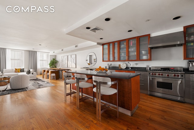 kitchen with wall chimney exhaust hood, a kitchen island, designer stove, and hardwood / wood-style floors