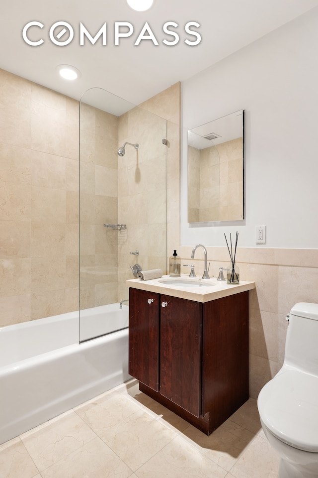 full bathroom with toilet, tiled shower / bath combo, vanity, and tile walls